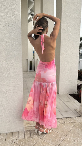Woman wearing a pink floral dress standing against a white wall.