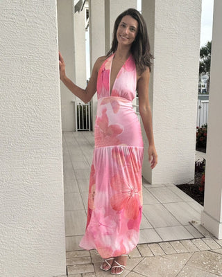 Woman wearing a pink tie-dye dress standing in front of a white wall.
