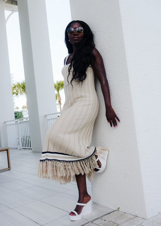Woman in a beige dress with fringe standing against a white column.