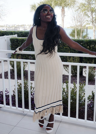 Woman in a white dress with black trim standing on a balcony with greenery in the background