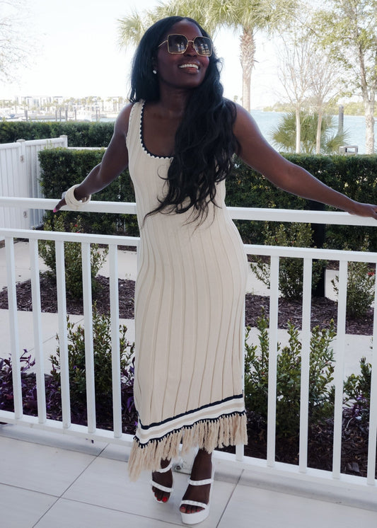 Woman in a white dress with black trim standing on a balcony with greenery in the background