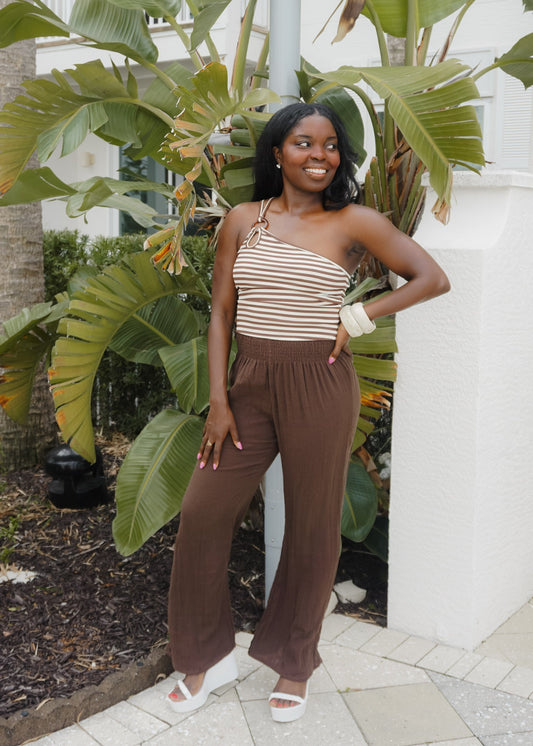 Woman in a striped top and brown pants standing in front of tropical plants.
