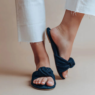 Navy blue knotted sandals worn with white pants on a neutral background
