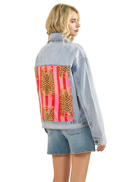 Person wearing a denim jacket with leopard patches  on a plain background