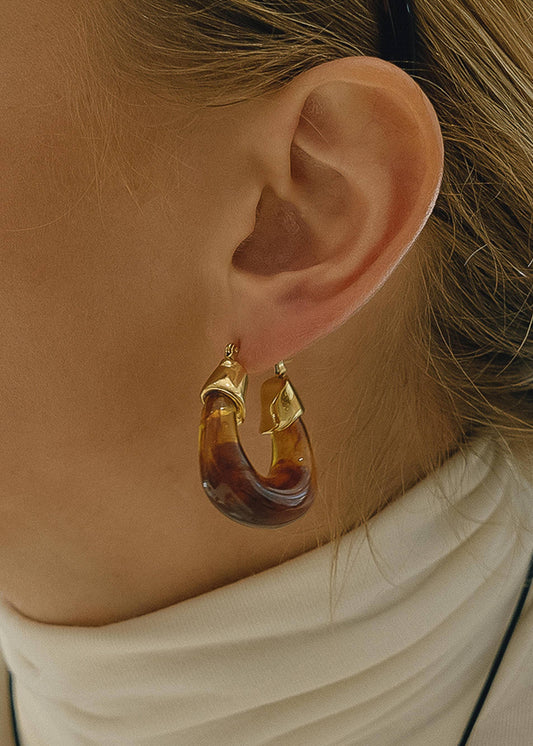 Close-up of an ear wearing a gold hoop earring with tortoiseshell design.