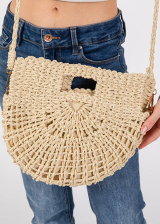 Beige woven handbag held by a person wearing blue jeans on a white background
