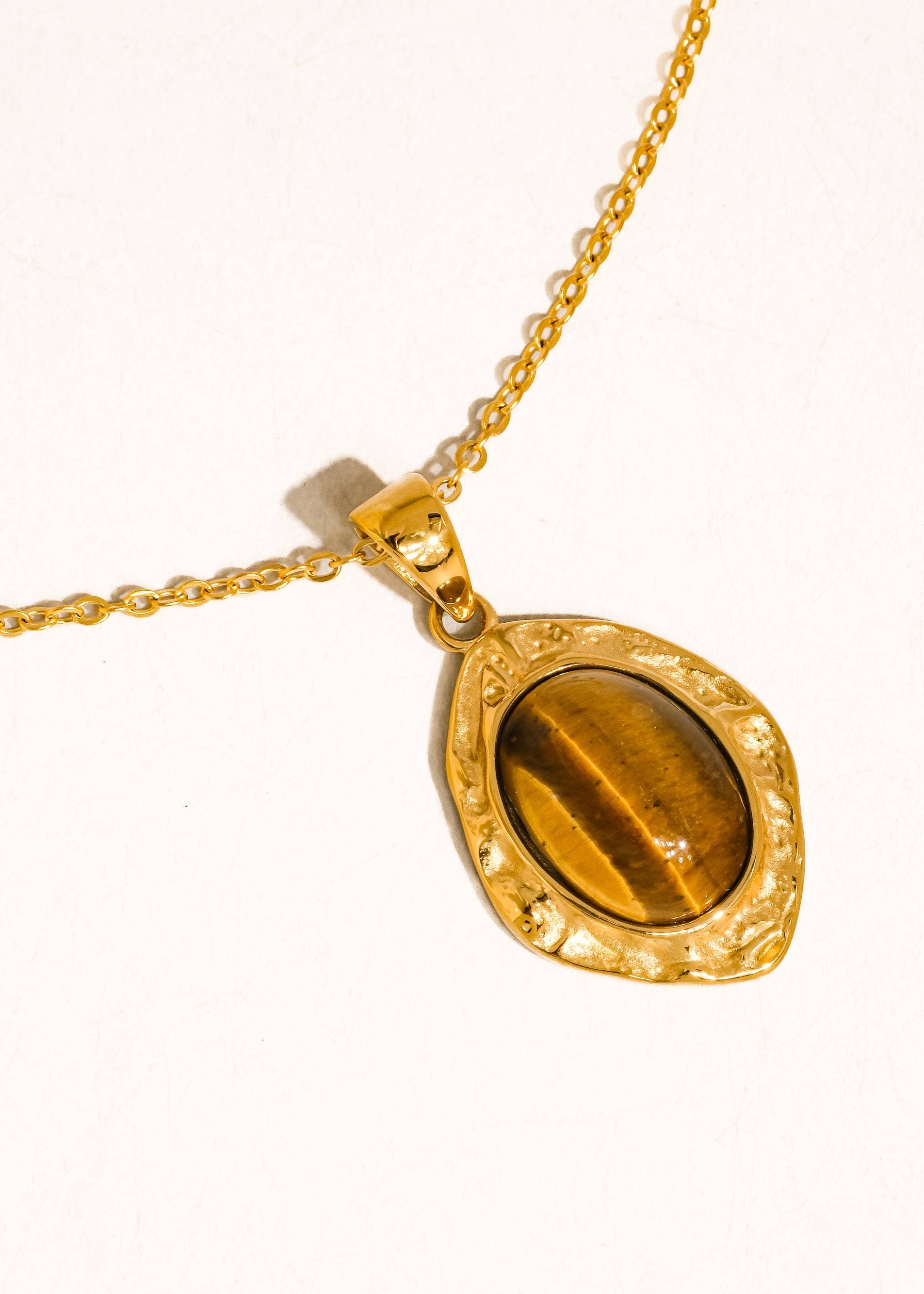 Gold necklace with a tiger's eye pendant on a white background