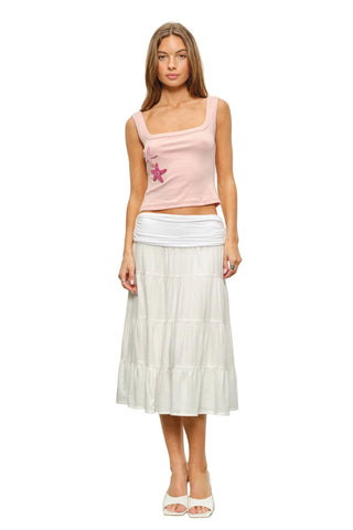 Woman wearing a pink top with a star design and a white skirt against a plain background