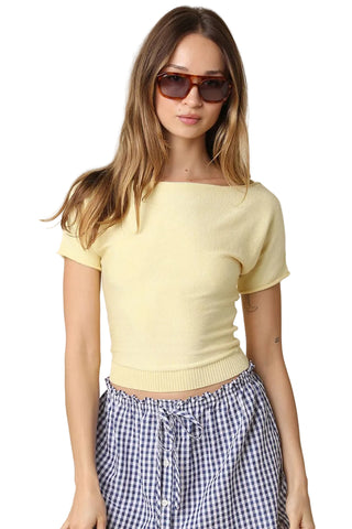 Woman wearing a yellow top and checkered pants against a beige background