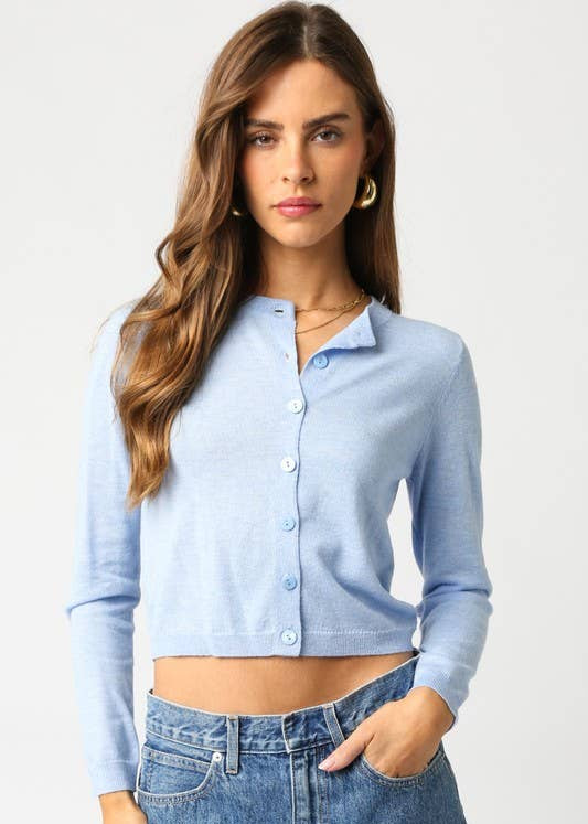 Woman wearing a light blue cardigan over a crop top and jeans on a white background