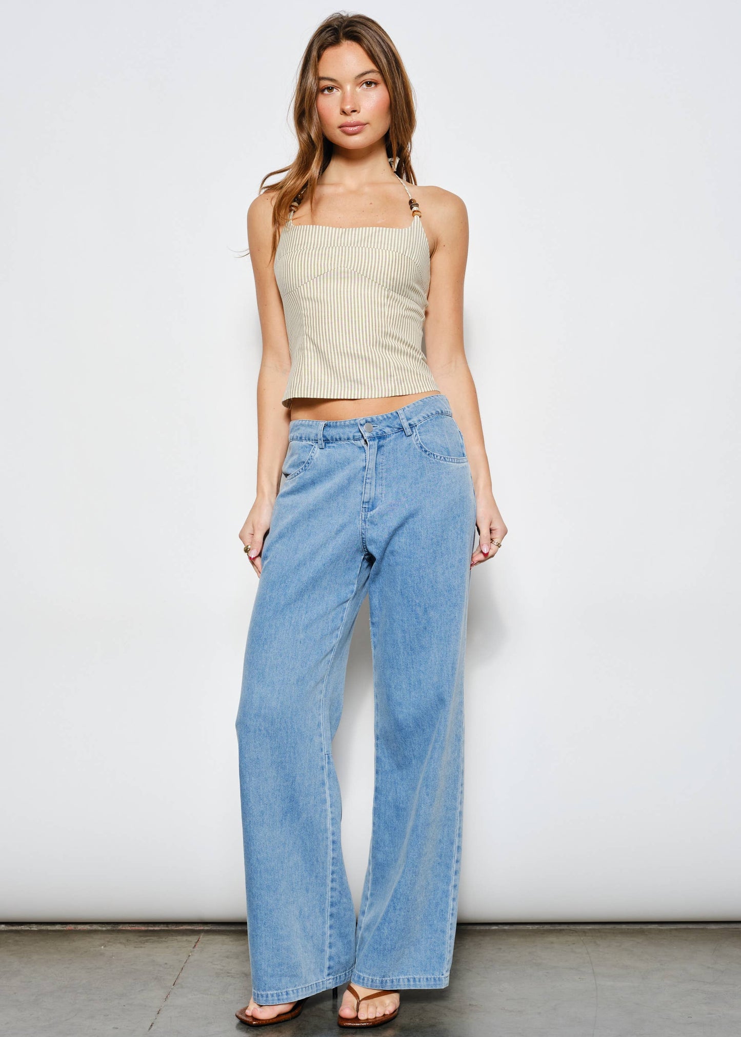 Woman wearing a beige top and light blue jeans against a white background