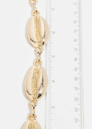 Gold shell bracelet with a ruler for scale on a white background