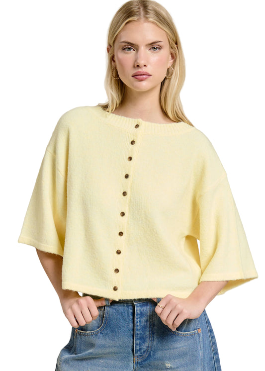 Woman wearing a yellow button-up top and blue jeans against a beige background