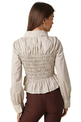 A woman shown from the back wearing a cream and brown vertically striped smocked blouse with a peplum hem, paired with dark brown pants, against a solid beige background.