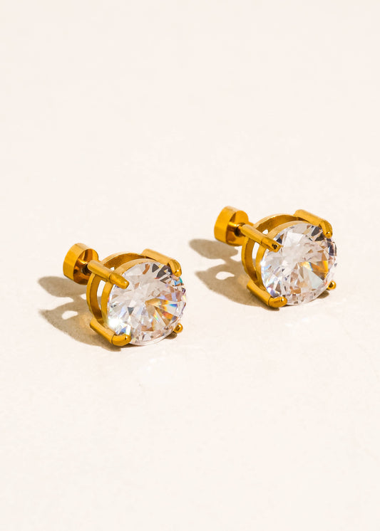 Gold stud earrings with clear gemstones on a beige background