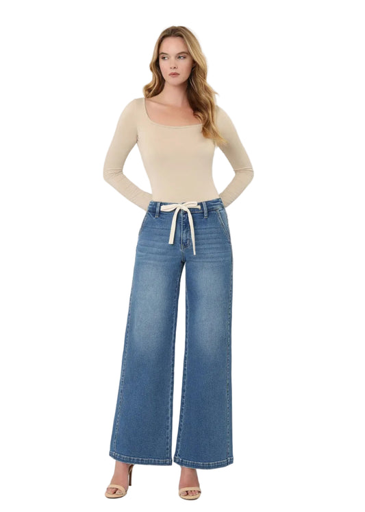 Woman wearing a beige top and blue jeans on a white background