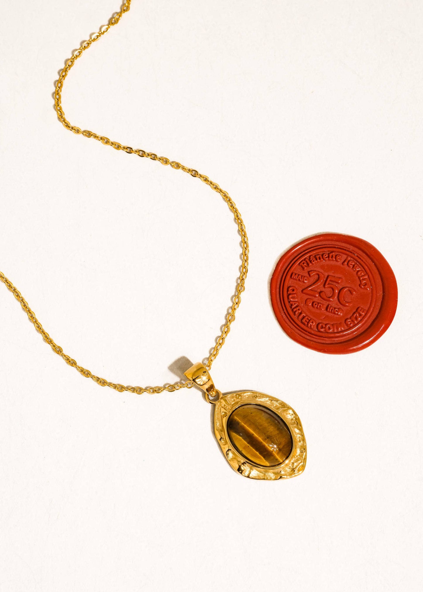 Gold necklace with a pendant and a red wax seal on a white background