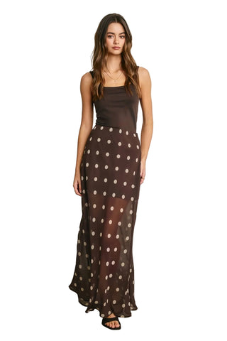 Woman wearing a brown sleeveless top and polka dot skirt against a plain background