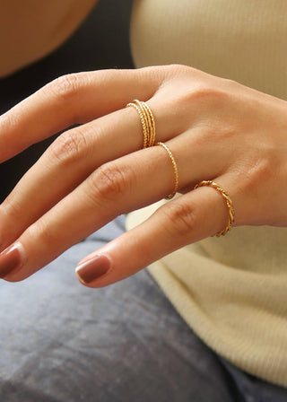 Close-up of a hand wearing multiple gold rings with a blurred background
