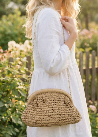 Woman in a white dress holding a woven handbag in a garden setting
