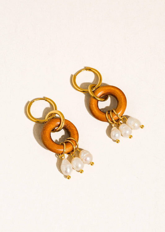 Pair of earrings with gold and brown links and pearl charms on a beige background