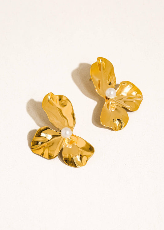 Gold butterfly earrings with pearl centers on a beige background