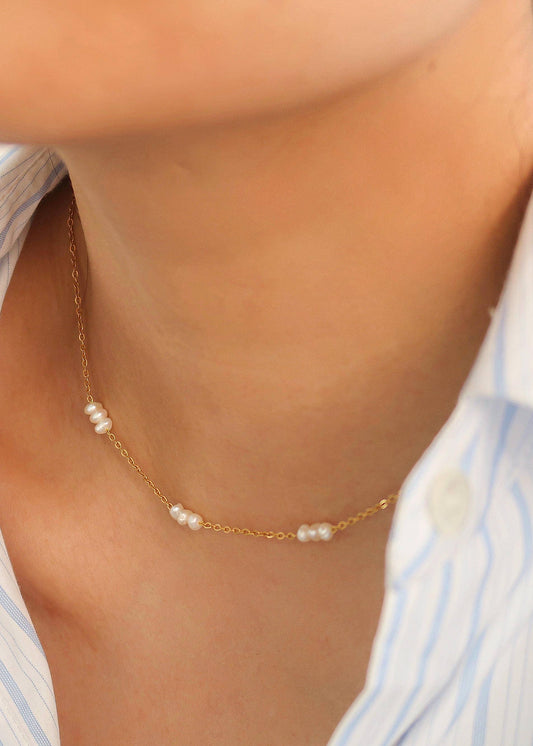 Gold necklace with pearls worn by a person in a striped shirt
