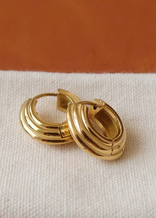Gold hoop earrings on a textured beige surface with a brown background