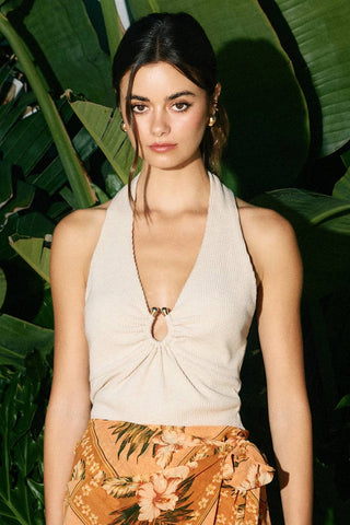 Woman wearing a beige halter top and floral pants against a green leafy background