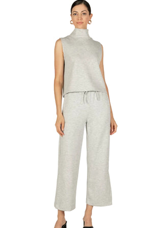 A model wearing a sleeveless turtleneck top and wide leg pants in gray, with side binding details and ankle length, paired with a waist tie.