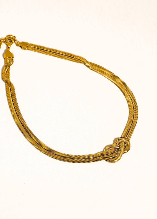 Gold bracelet with a knot design on a white background
