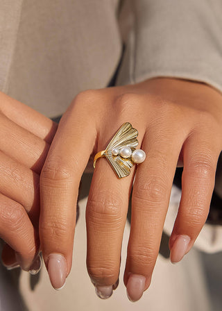 Gold ring with pearls on a hand against a neutral background