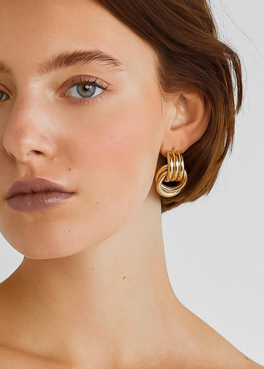 Close-up of a woman wearing gold hoop earrings against a neutral background
