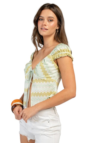 Woman wearing a patterned top and white shorts on a plain background