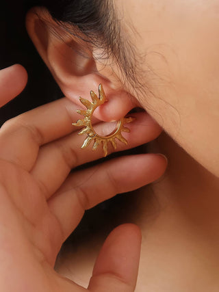 A close-up of a person wearing a small gold crescent moon hoop earring with sunburst details, with their hand gently touching the earring.