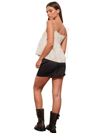 Woman wearing a white top and black skirt with boots on a plain background