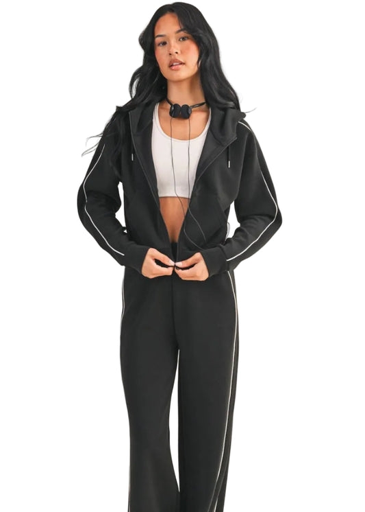 Woman wearing a black tracksuit with white piping on a beige background